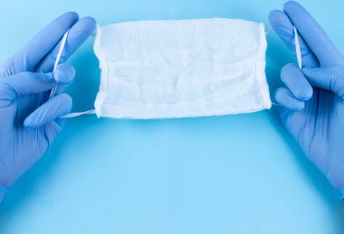 Eldivenli eller mavi arka planda antivirüs maskesi tutuyor. Salgına karşı koruma, havadan bulaşan hastalıklar, SARS, grip. Metin için yer