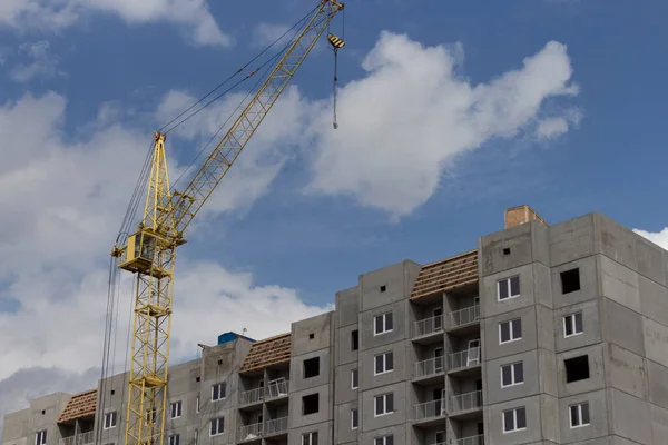 İnşaat alanı. Vinçli bir inşaat alanı. Mavi gökyüzü ve bulutlara karşı inşaat halindeki beton gri bir bina..