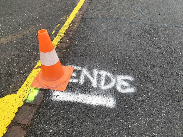 Traffic cone next to road boundary on the German word Ende written in white and underlined.