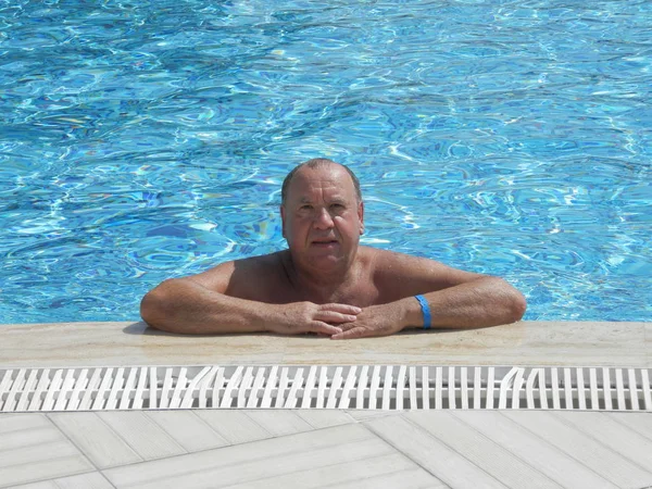 A man is resting on the wall of the pool after a swim.
