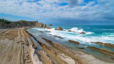 Rocky shore landscape at low tide, Northern Spain. Cliffs flooded with water, the ocean with a tidal wave, cliff, blue sky with clouds.