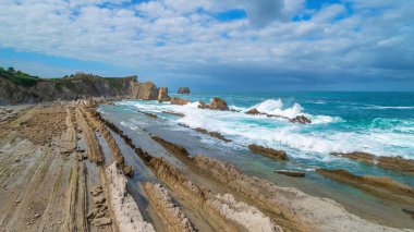Rocky shore landscape at low tide, Northern Spain. Cliffs flooded with water, the ocean with a tidal wave, cliff, blue sky with clouds. clipart