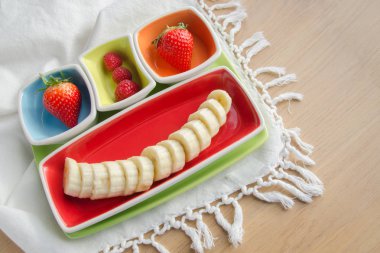 Pencere ışığında beyaz masa örtüsü üzerinde taze meyveler.