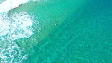 Temiz mavi suyun üzerinden yukarı doğru yükselen hava akımı sörfçüleri kıyıya doğru el sallıyor.