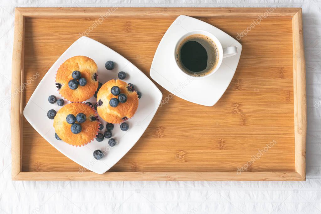 Wooden tray on the bed. Blueberry cupcakes and cup of coffee. Perfect breakfast and start of the day. Top view