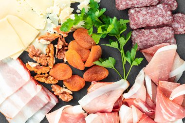 Peynirli peynir tabağı, prosciutto, fındık. Sağlıklı yiyecekler, süt ürünleri, peynir ve et. Aperatifler: jambonlu parmesan peyniri, salam, siyah tabakta sosis.