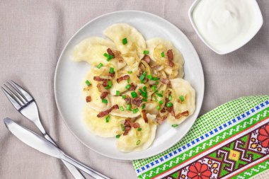 Kızarmış soğan ve pastırmalı ev yapımı hamur tatlısı. Geleneksel olarak, Ukrayna yemeği yeşil soğan ve Ukrayna havlusuyla süslenir. Masada köfteli ve ekşi kremalı tabak. Üst görünüm