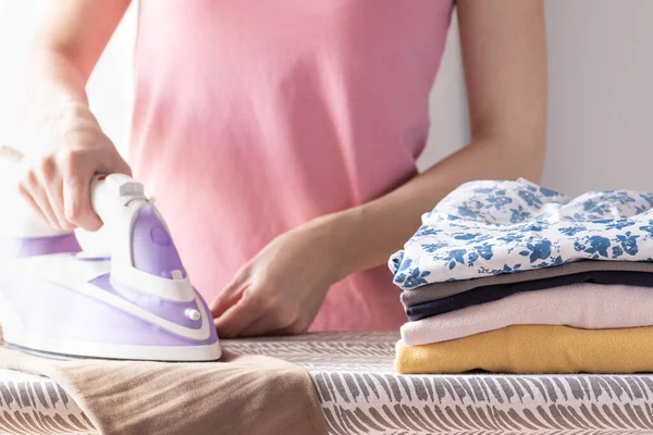 Woman irons washed clothes in room during homework. Ironing with colored iron clean clothes.
