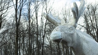 Halka açık bir parkta koruyucu maske takan beyaz bir geyik heykeli.