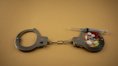 Uyuşturucu bağımlılığını simgeleyen ilaçlarla kelepçelenmiş.