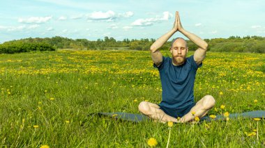 Sakallı kel bir adam meditasyon yapıyor.
