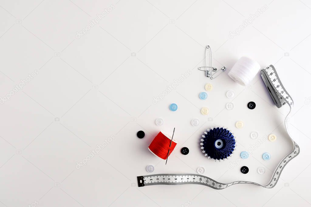 measuring tape, yarns, needles, safety pins, buttons, arranged on white background