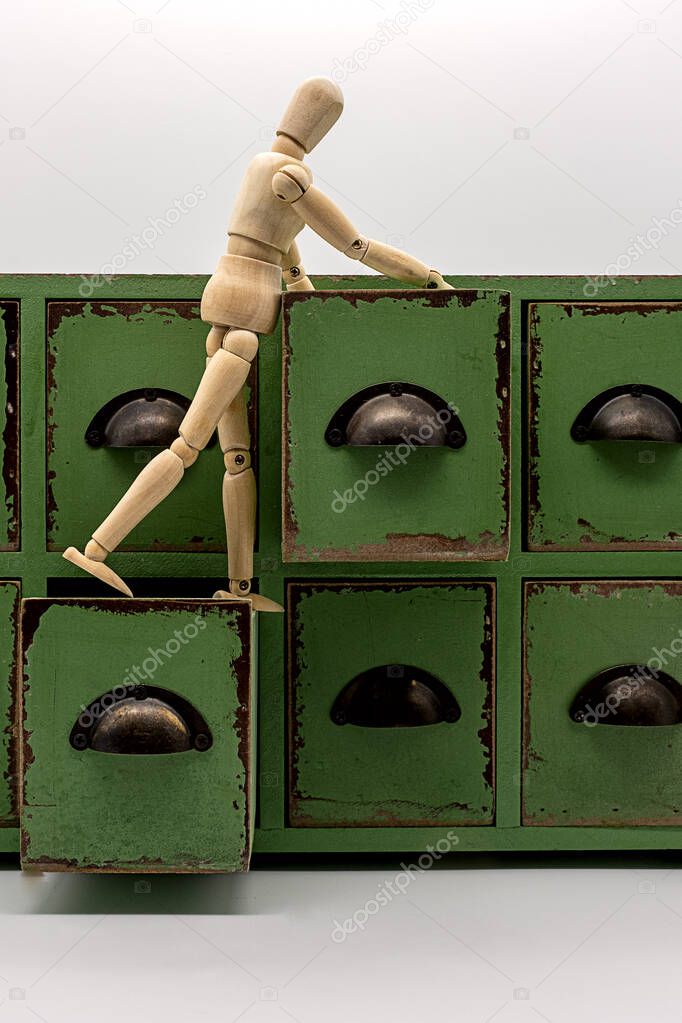 a wooden doll stands on two open drawers of a small chest of drawers and is looking for something