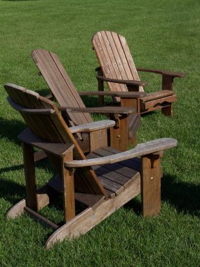 Güneşli bir günde çimenli bir çimenlikte bir grup kahverengi Adirondack şezlongunun yakın görüntüsü