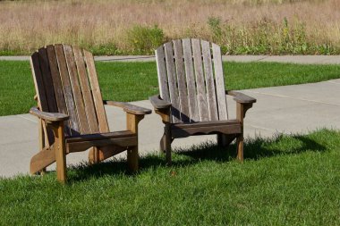 Güneşli bir günde çimenli bir çimenlikte bir çift kahverengi Adirondack şezlongunun yakın görüntüsü