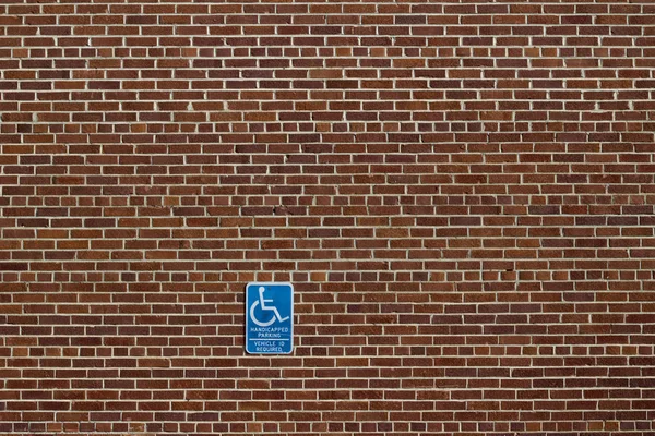 Shabby chic older red brown brick wall texture background in common bond brickwork pattern, with weathered appearance, showing a handicap parking sign