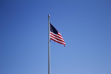 Derin mavi gökyüzü arka planına sahip bayrak direğinde Amerikan Yıldızları ve Şeritleri görüntüsü