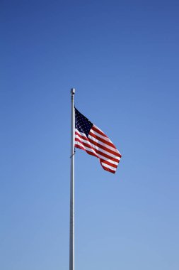 Derin mavi gökyüzü arka planına sahip bayrak direğinde Amerikan Yıldızları ve Şeritleri görüntüsü