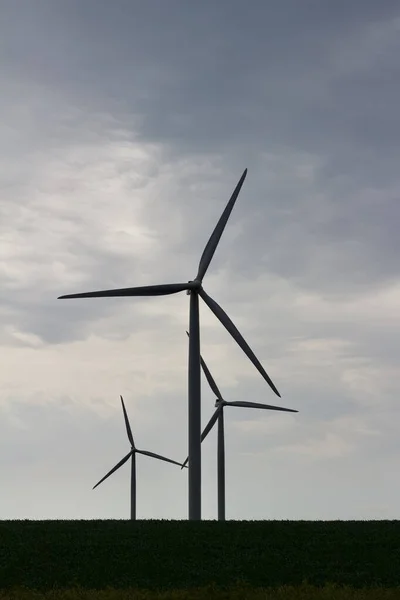 Upward silhouette of three giant wind turbines on an agricultural field with overcast sky