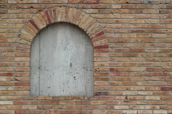 Boarded up arched brick window on a colorful antique brick wall texture background, with hot pepper colored bricks in shades of beige, red, white, yellow, and brown