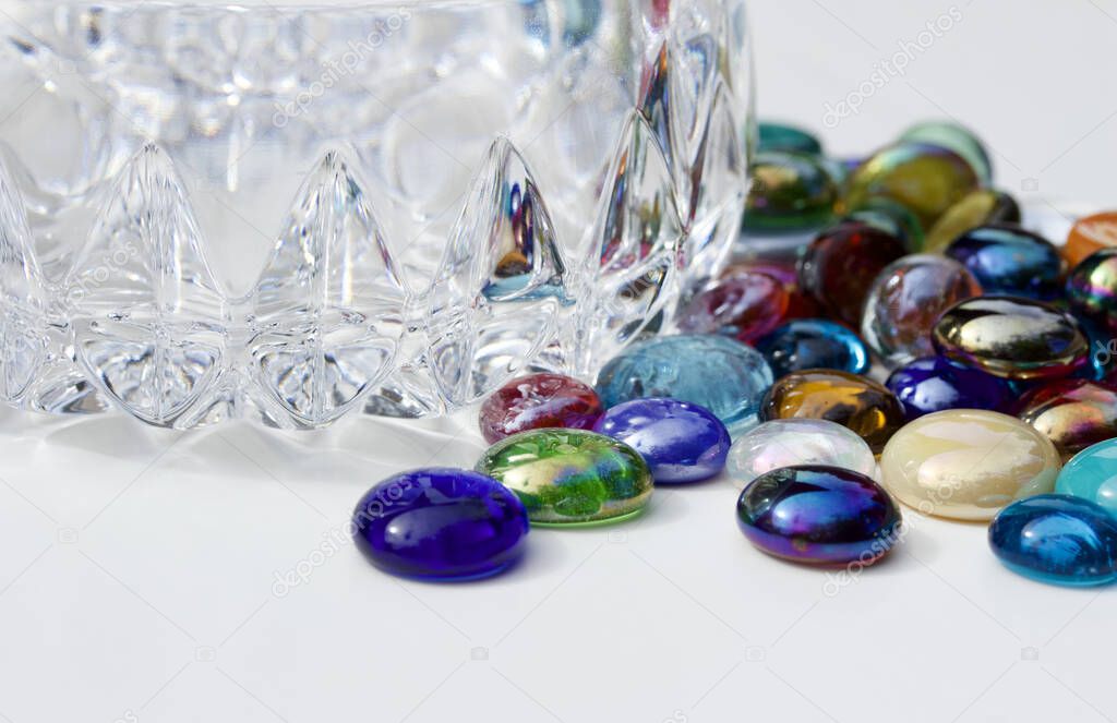 Close up view of a small crystal glass bowl surrounded with colorful glass bead dragon tears, on white background