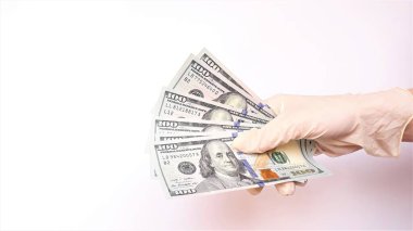 Tıbbi eldivenli eller beyaz arka planda bir tomar dolar tutuyor. Para enfeksiyonu, kirli para salgını, COVID-19, ödenmiş ilaç, tedavi ücretleri, rüşvet, yasadışı ameliyat.