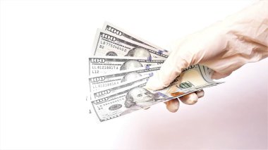 Tıbbi eldivenli eller beyaz arka planda bir tomar dolar tutuyor. Para enfeksiyonu, kirli para salgını, COVID-19, ödenmiş ilaç, tedavi ücretleri, rüşvet, yasadışı ameliyat.