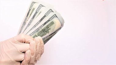 Tıbbi eldivenli eller beyaz arka planda bir tomar dolar tutuyor. Para enfeksiyonu, kirli para salgını, COVID-19, ödenmiş ilaçlar, tedavi ücretleri, rüşvetler, yasadışı ameliyatlar..