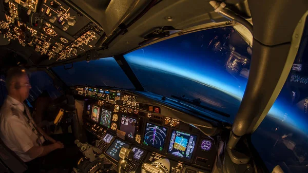 Pilot, modern jet yolcu uçağı uçuş güvertesinde çalışıyor. Kokpitten güzel manzara, uçuş ve seyrüsefer enstrümanı ışıkları karartılmış ve açık gökyüzünün olduğu bir gecede doğal mavi saat.