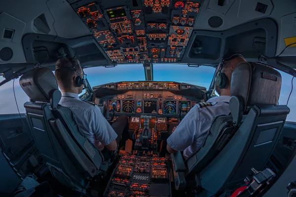 Pilots in the cockpit of jet commercial airplane during the flight with first rays of the warm sunrise entering through the flight deck window