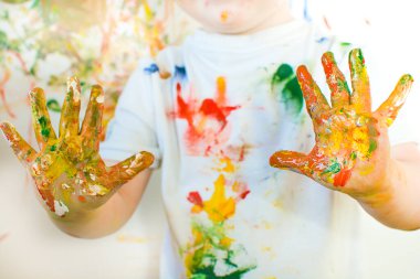Çocuğun elleri renkli boyayla lekelenmiş. Çocuk elleriyle duvara resim çiziyormuş. Çerçeve kırpılmış, yakın plan..
