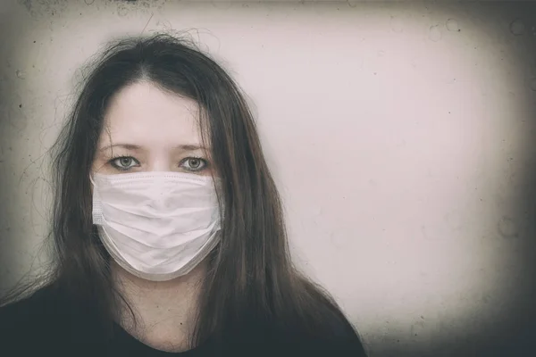 A woman in a medical mask looks into the frame. Prevention of coronavirus infection. The photo is artistically processed.