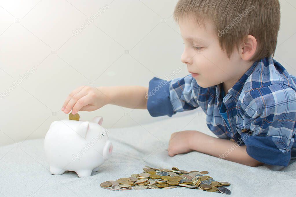 A preschooler puts a huge pile of coins in the piggy Bank. The child is lying on his stomach. Photo concept to teach your child to save money. The photo is artistically processed.