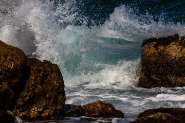 Kıyı kayalıklarında köpük ve spreyle sörf dalgaları kopuyor..