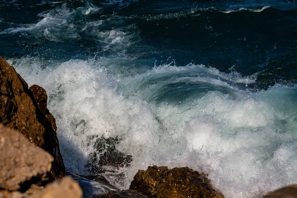 泡とスプレーで海岸の岩に波の波が打ち寄せる — ストック写真