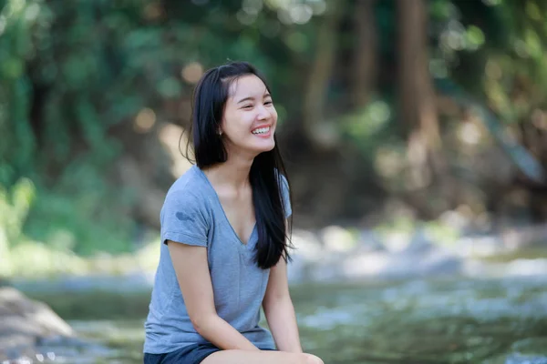 Dívka sedí u vodopádu a usmíval se šťastný, měkké zaostření — Stock fotografie