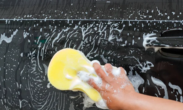 hand of Man washing the car using the yellow sponge with foam