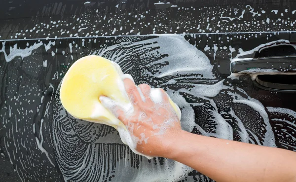 hand of Man washing the car using the yellow sponge with foam