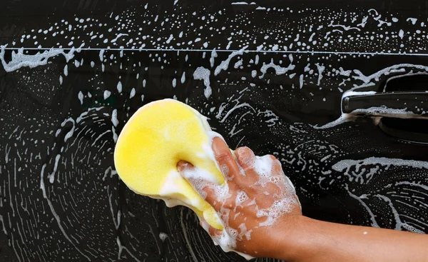 Homem lavando o carro usando a esponja amarela com espuma  . — Fotografia de Stock