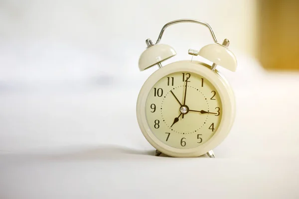 Reloj despertador analógico en cama blanca, hora en la mañana con un calabozo —  Fotos de Stock