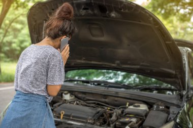 Asyalı kadın cep telefonunuzun ve kırık aşağı arabaya bakarken 