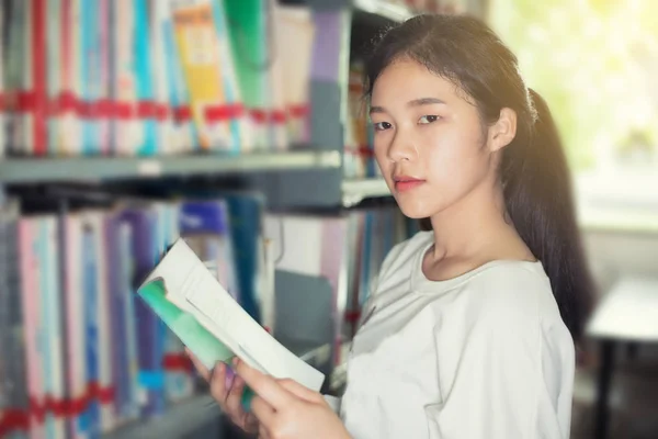 Asiática mujer estudiantes holding para selección libro en biblioteca — Foto de Stock