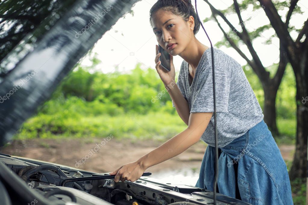 Asian woman using mobile phone while looking at broken down car 