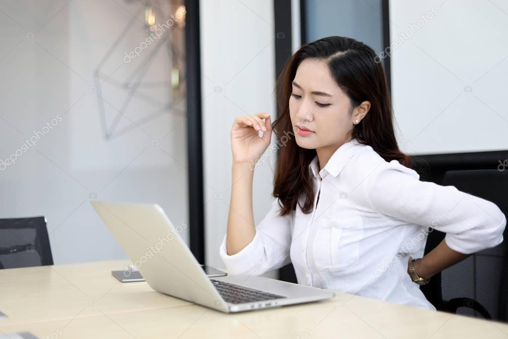 Asian Business women with back pain sin an office and working ha