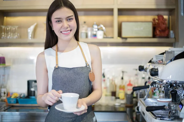 Азіатські жінки Barista посміхається і проведення чашку кави і за допомогою mac — стокове фото