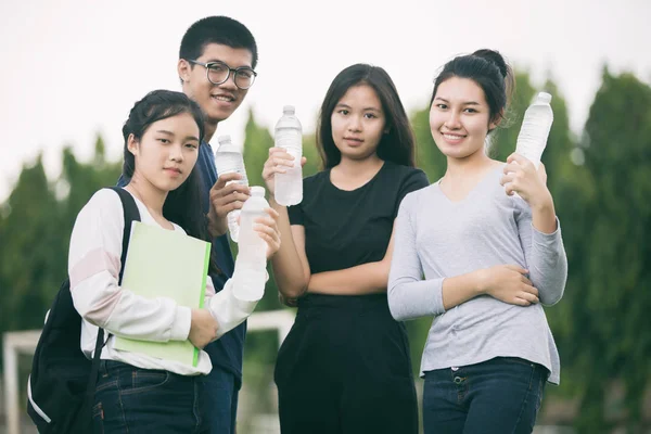 Азиатская группа студентов держит бутылку воды на лужайке кампуса — стоковое фото