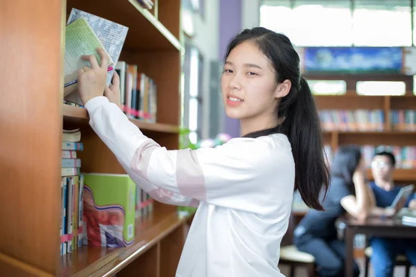 Asiática mujer estudiantes holding para selección libro en biblioteca — Foto de Stock