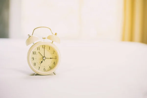 Reloj despertador analógico en cama blanca, hora de la mañana con un calabozo —  Fotos de Stock