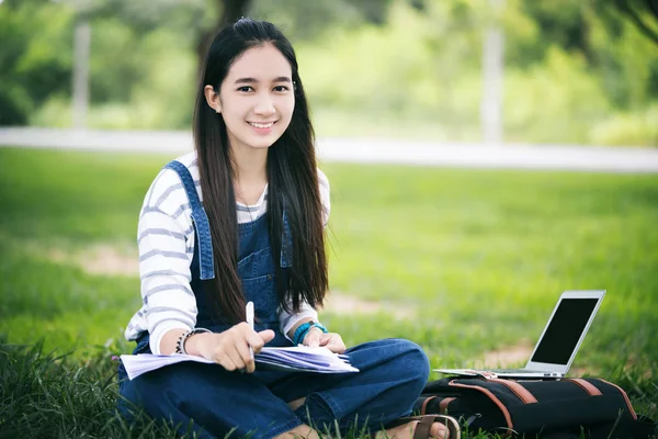 Sorrindo bela menina asiática lendo livro e trabalhando na árvore em — Fotografia de Stock