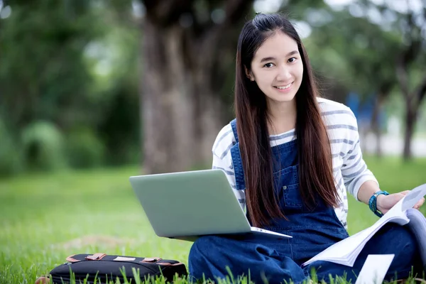 Sonriendo hermosa chica asiática leyendo libro y trabajando en el árbol en —  Fotos de Stock
